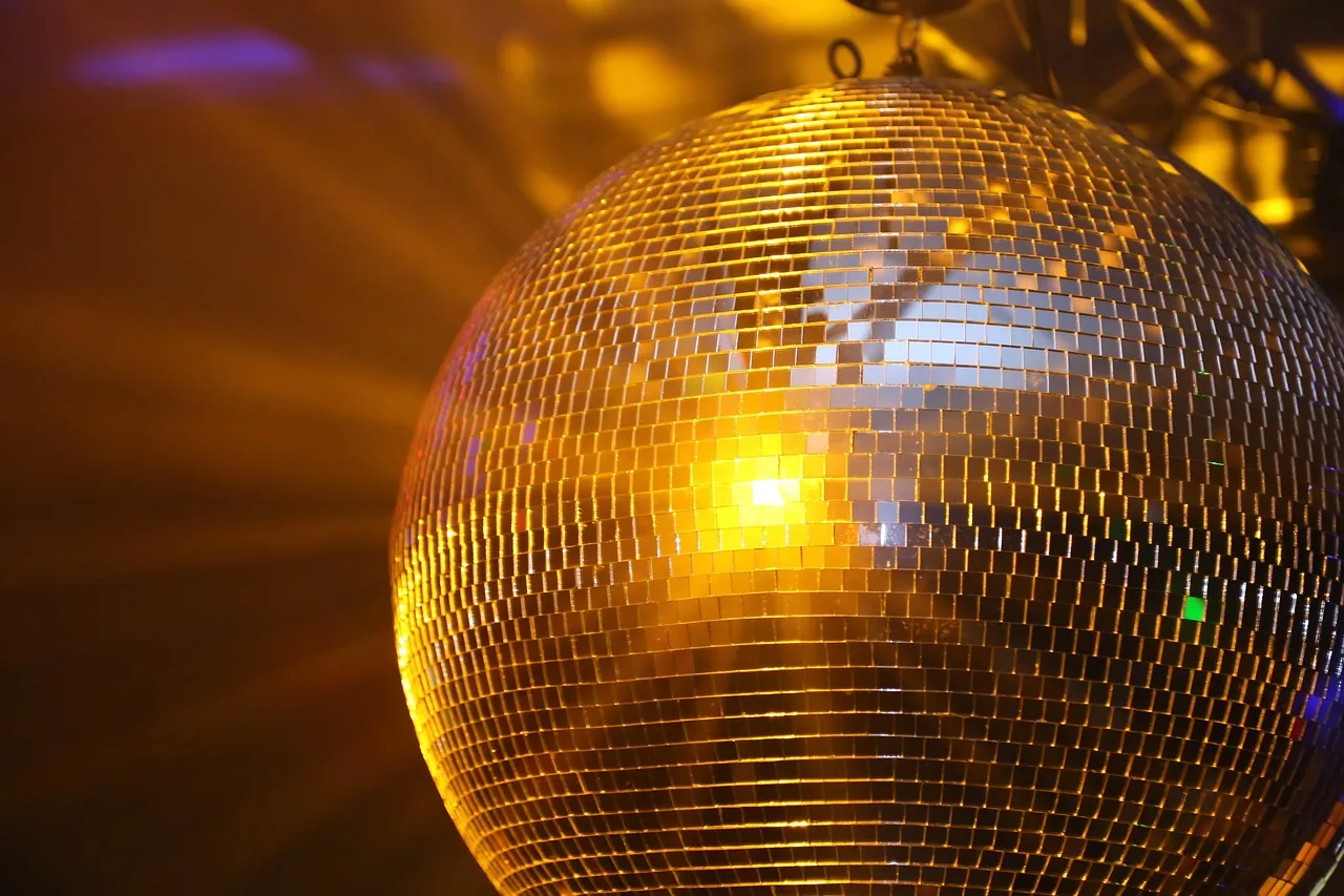 A large mirrored disco ball reflects warm golden light against a dark background.